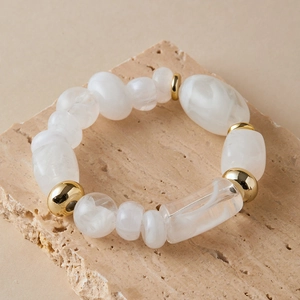 Detailed shot of beaded bracelet with white marble patterns on a beige stone base