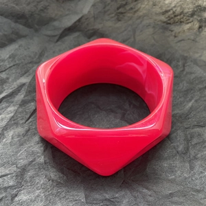 Dettaglio di un ampio bracciale in resina magenta con design esagonale moderno