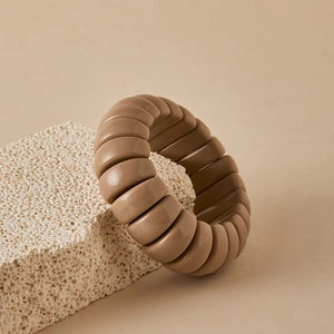 Detail view of a segmented brown resin bracelet on a textured natural stone stand