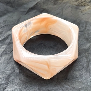 Dettaglio del bracciale esagonale in resina marmorizzata rosa e bianca su grigio