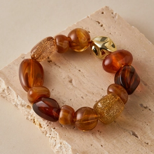 Detailed close-up of mixed amber resin beads and irregular gold metal bead on stone surface