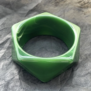 Dettaglio di un bracciale esagonale largo in resina marmorizzata verde scuro su sfondo