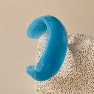 Close-up of a sky blue acrylic cuff bangle with marble texture on a white stone base