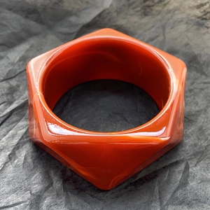 Dettaglio di bracciale esagonale in resina con trama marmorea arancione su sfondo scuro