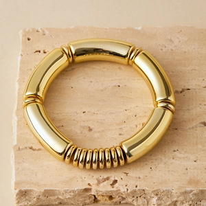 Polished gold elastic bracelet featuring curved tube links on a natural stone background