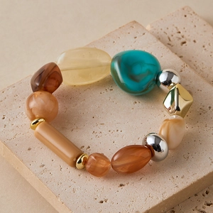 Detail of beach style beaded bracelet with blue resin and metallic charms on stone