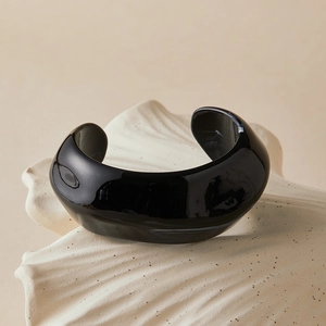 Minimalist thick open cuff bracelet in black acrylic on a neutral wavy background