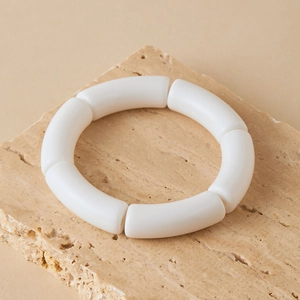 Close-up van matte crème acryl gebogen buisarmband op een decoratieve stenen basis