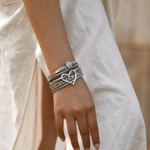 Detail van een bohemien meerlaagse armband met hartvormige hanger en glitterkristal op de pols