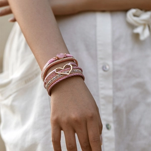 Boheems gelaagde armband met roze koord en gouden hartje gedragen om de vrouwelijke pols