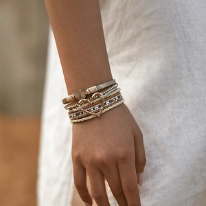 Detail van boho gelaagde armband met beige leer, gouden hartje en fonkelende strass