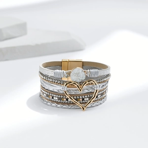 Detail eines mehrlagigen Wickelarmbands mit goldenem Herzanhänger und Magnetverschluss