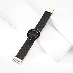Dettaglio di bracciale multistrato in pelle nera con fibbia dorata e chiusura magnetica
