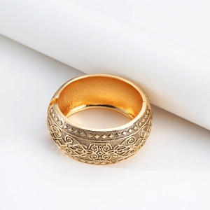 Dettaglio del bracciale rigido dorato largo con rilievo floreale vintage e chiusura