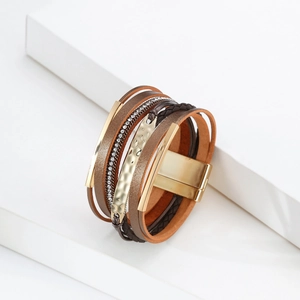 Détail d'un bracelet multicouche en cuir bohème avec fermoir magnétique et plaque dorée ondulée