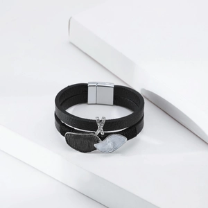 Detail of multi-layer black leather bracelet featuring rhinestone X charm and leaf pendant