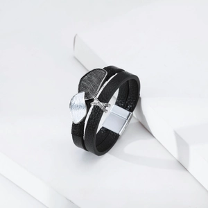 Detail of layered black leather bracelet with leaf charms and rhinestone X buckle