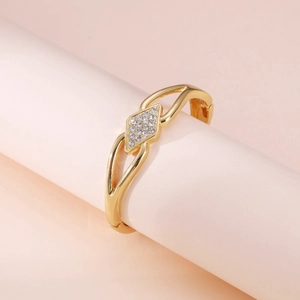 Detail of a gold hinged bangle featuring a diamond-shaped centerpiece set with white zircon