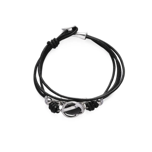 Detalle de pulsera de cuero trenzado negro de varias capas con dijes de metal plateado y cierre