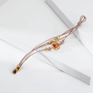 Detalle de una pulsera multicapa de cuero rosa con cuentas doradas y colgante ámbar