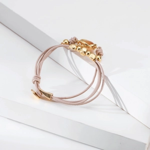 Detalle de una pulsera multicapa con cordones rosas, cuentas doradas y hebilla de metal
