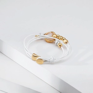 Detalle de pulsera multicapa de cuero blanco con cuentas doradas y piedra de cristal rosa