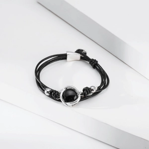 Detalle de pulsera de cuero negro multicapa con adornos plateados y piedra negra