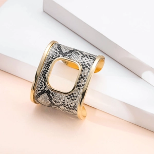 Dettaglio di un bracciale a fascia dorato con texture a serpente e ritaglio centrale