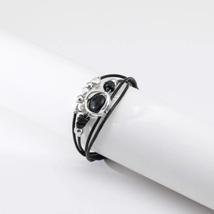 Detalle de una pulsera multicapa de cuero negro con cuentas plateadas y gema negra