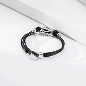 Vista de detalle de la pulsera de cuero negro multicapa con cuentas plateadas y cierre en T