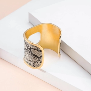 Dettaglio del bracciale rigido dorato con trama a pelle di serpente grigia e ritaglio