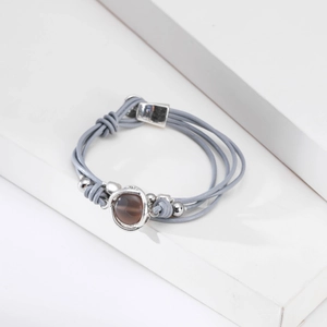 Detalle de pulsera de cuero gris de varias capas con cuenta marrón y bolas de plata