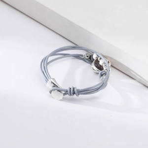 Detalle de la pulsera de cuero gris multicapa con acentos plateados en podio blanco