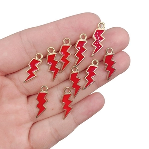 Handheld view of ten red enamel lightning bolt charms with gold metal edges for DIY jewelry