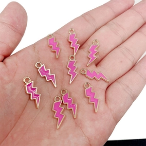 Macro view of a gold lightning bolt charm with pink enamel inlay on palm for size scale