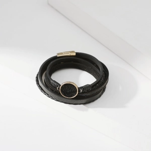 Dettaglio del bracciale multistrato in pelle nera con anello dorato e trama in pelo di pony