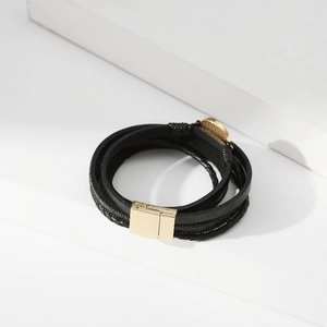 Dettaglio di un bracciale multistrato in pelle nera con chiusura magnetica in oro lucido