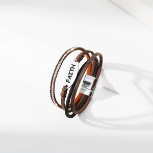 Detail eines mehrlagigen Lederarmbands mit silbernem Faith-Anhänger und Magnetverschluss