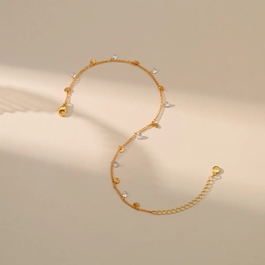 Elegante tobillera bañada en oro de 18K con circonitas y discos dorados sobre fondo beige