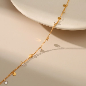 Collar de oro minimalista con lentejuelas y circonitas sobre un fondo beige cálido