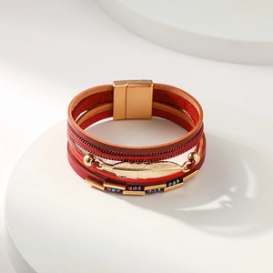 Détail d'un bracelet multicouche en cuir rouge avec breloque plume dorée et fermoir aimanté