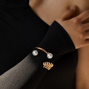 Elegant gold cuff bracelet with pearls and leaf design on wrist with black sweater