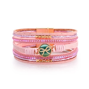 Dettaglio del bracciale multistrato in pelle rosa con strass e ciondolo a fiocco dorato