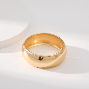 Detailed close-up of a wide golden open cuff bracelet with a polished mirror finish surface