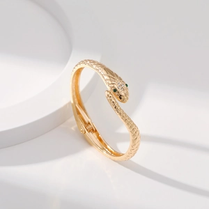 Bracciale a serpente dorato con occhi di pietre verdi e cristalli lucenti su sfondo bianco