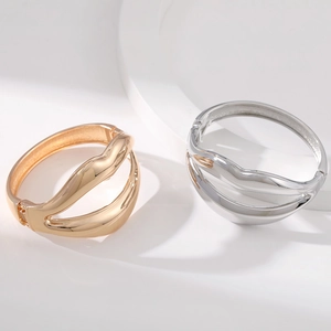 Polished gold and silver alloy wave bangles with artistic cutout design on white podium