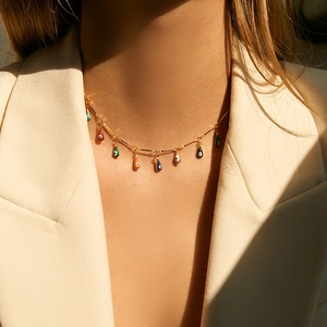 Gold chain necklace with colorful enamel teardrop evil eye charms on a model in sunlight