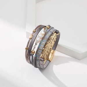 Détail d'un bracelet bohème multicouche en cuir avec breloque plume dorée et fermoir aimanté