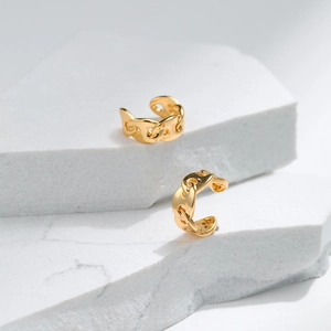 Polished 18K gold pig nose chain link ear cuffs displayed on a white stone pedestal