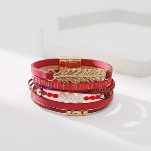 Détail d'un bracelet multicouche en cuir rouge avec pendentif plume dorée et perles